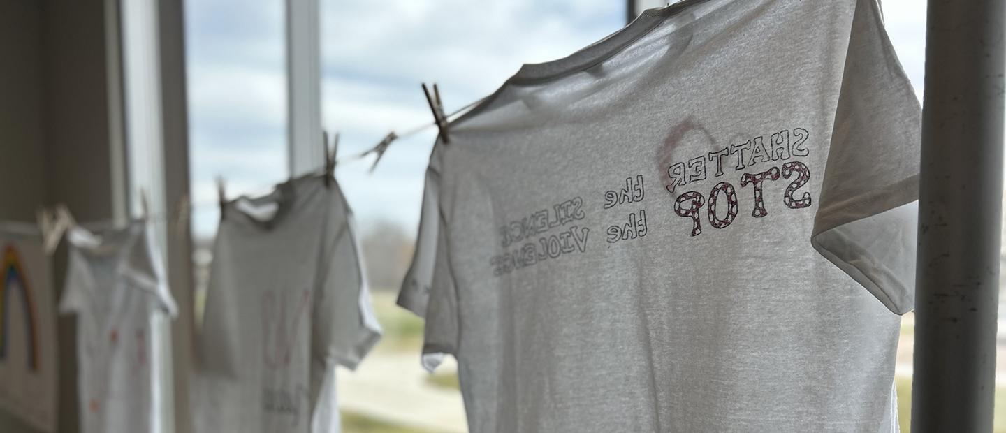 Photo of t-shirts on clothes line. T-shirt reads stop the violence, shatter the silence